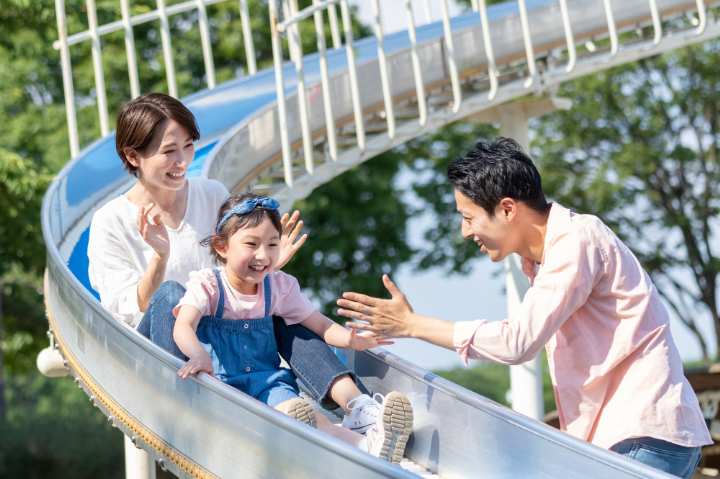 滑り台を滑る母娘と笑顔で見守る父親
