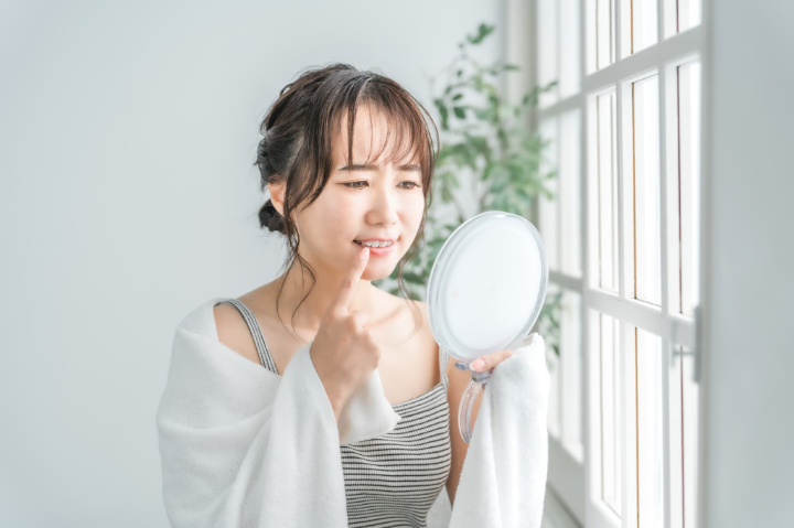 後戻りした歯を鏡で見て眉をしかめる女性