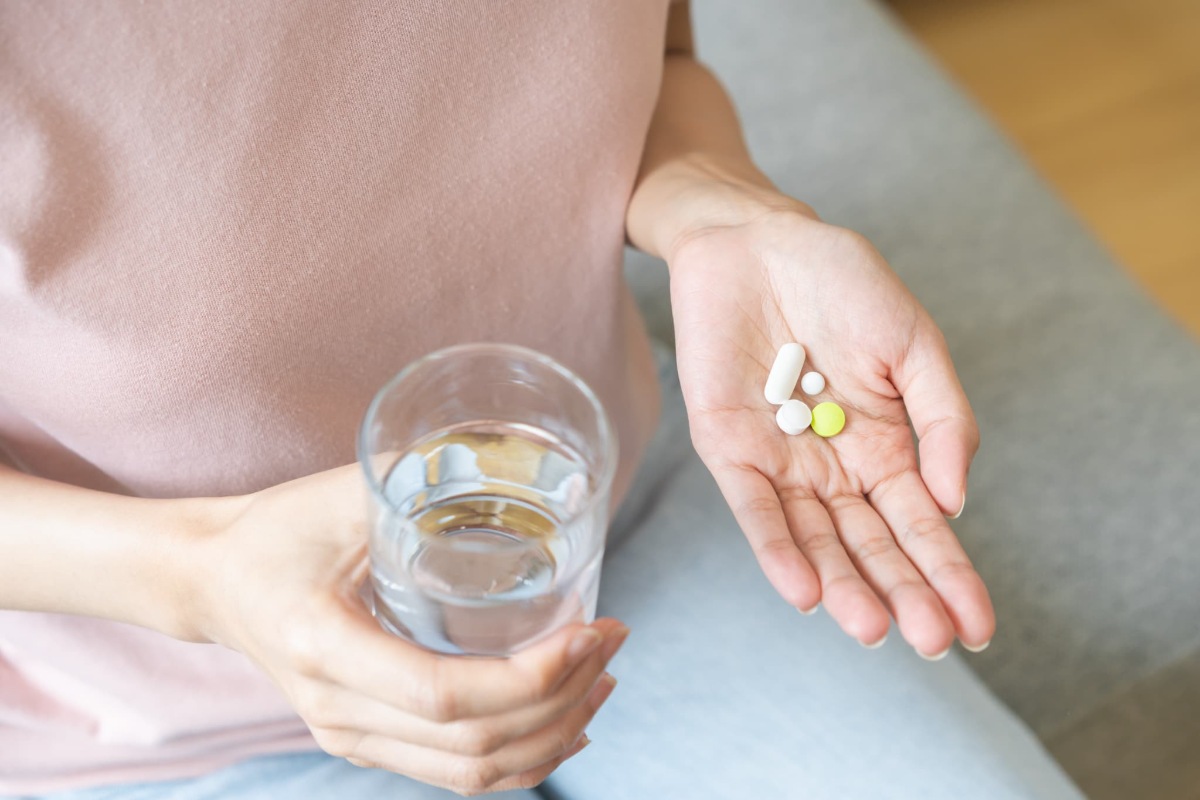 手に鎮痛剤と水の入ったコップを持った人